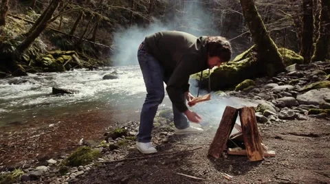 Man Building a Fire Next to a river Stock Footage 52330682