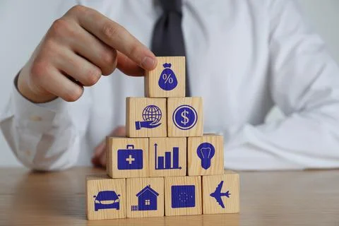 Man building pyramid of cubes with different icons at wooden table, closeup.  Fotos de archivo