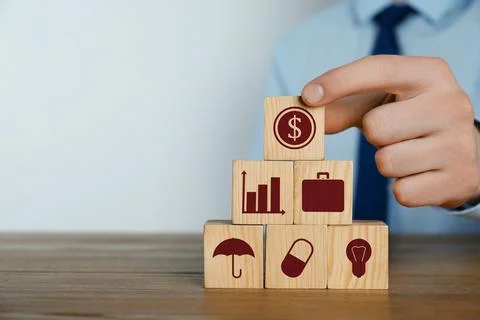 Man building pyramid of cubes with different icons at wooden table, closeup.  Fotos de archivo
