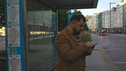 A man at a bus stop is talking on the phone. Morning no people, work outside the Stock Footage 220787493