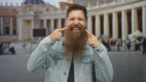Man with bushy beard in denim jacket pushes his cheeks with fingers in busy.. Stock Footage 313453871