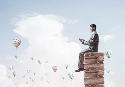 Man businessman on stack reading book and aerostats flying aroun 库存照片
