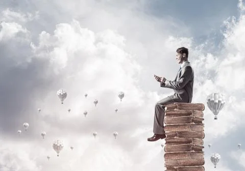 Man businessman on stack reading book and aerostats flying aroun 库存照片