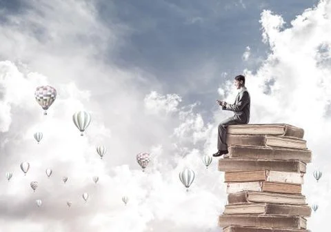 Man businessman on stack reading book and aerostats flying aroun 库存照片