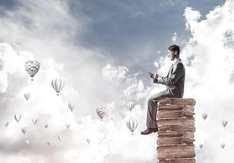 Man businessman on stack reading book and aerostats flying aroun 库存照片
