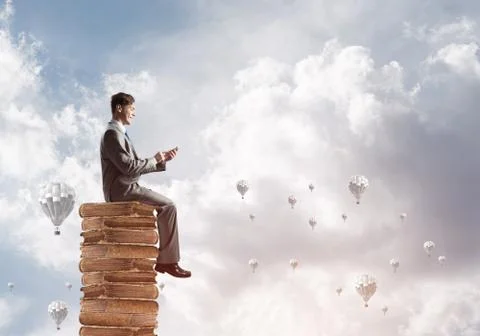 Man businessman on stack reading book and aerostats flying around Foto stock