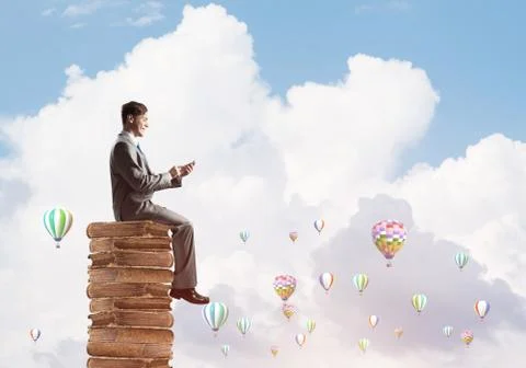 Man businessman on stack reading book and aerostats flying around 库存照片