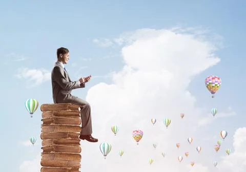 Man businessman on stack reading book and aerostats flying around Foto stock