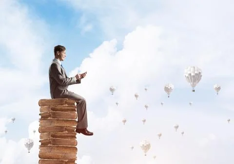 Man businessman on stack reading book and aerostats flying around 库存照片