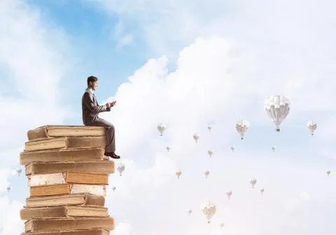 Man businessman on stack reading book and aerostats flying around 库存照片