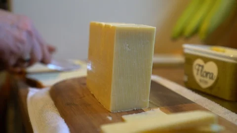 Man buttering white sliced bread to make cheese sandwich on wooden worktop, 4k Stock Footage 86985426