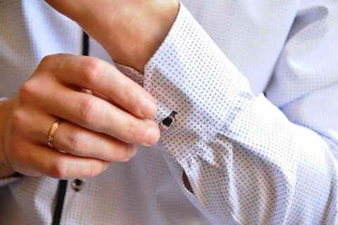 A man buttoning a button on the sleeve of a white shirt Stock Photos