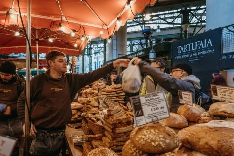 Man buying bread from Bread Ahead stall in Borough Market, London, UK, motion 스톡 사진