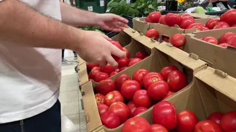 A man buys tomatoes in a vegetable store, chooses fresh vegetables in a sup.. Stock Footage 249386196