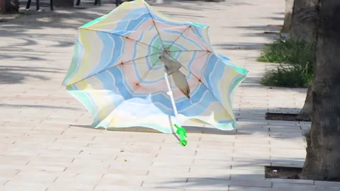 A man is caching rolling sun umbrella at beach promenade. Vídeo Stock 152701457