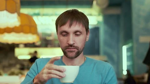 A man in a cafe, drinking coffee close - up, looking at the camera Stock Footage 99233895
