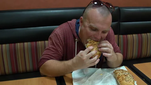 A man in a cafe sits at a table and eats a sandwich. Stock Footage 100616531