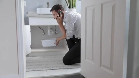 Man Calling  Emergency Plumber After Water Leak At Bathroom, Home Stock Footage 120893473