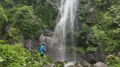 Man with Camera Admiring Waterfall in Lush Tropical Forest, Wide Shot Stock Footage 324850740