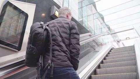 Man with camera and bag going up train station escalators out into the city Stock Footage 242393877