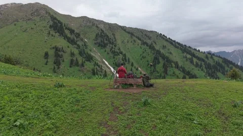 Man with camera captures scenic mountain landscape from grassy hilltop Stock Footage 336964656