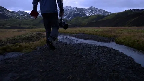 Man with camera walking over water stream towards mountains Stock Footage 74908101