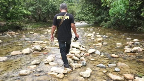 Man with camera walks through shallow stream Stock Footage 165507030
