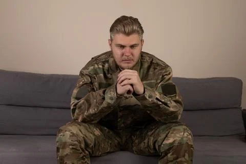 Man in camouflage sitting on a couch, holding a map and looking at a compass Stock Photos