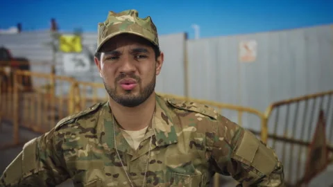 Man in camouflage uniform grimaces at construction fencing near building; d.. Stock Footage 314654854