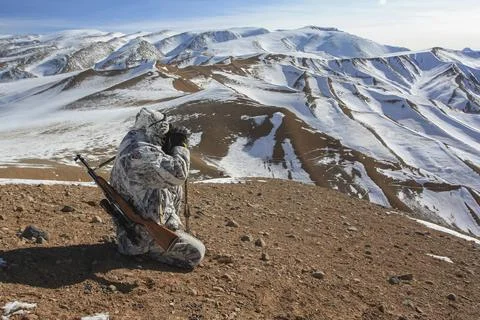 Man in camouflage wearing mask from wind and sun watches mountains through .. Stock Photos