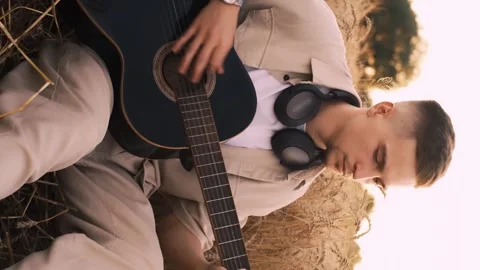 Man camper sitting on grass in field at sunset playing guitar singing song looki Stock Footage 250623558