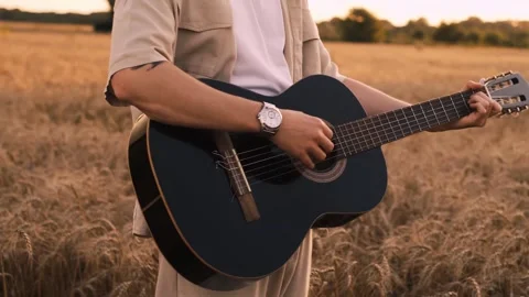 Man camper sitting on grass in field at sunset playing guitar singing song looki Stockbeeldmateriaal 250623772