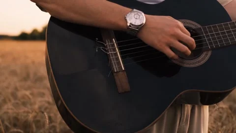 Man camper sitting on grass in field at sunset playing guitar singing song looki 스톡 동영상 250623785