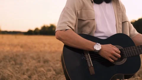 Man camper sitting on grass in field at sunset playing guitar singing song looki Video stock 250623792