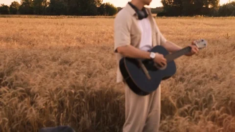 Man camper sitting on grass in field at sunset playing guitar singing song looki Vídeo Stock 250623815