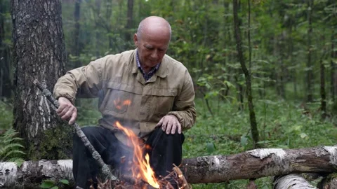 A man at a campfire in the forest. An old man looks at a forest fire in nature 스톡 동영상 168646548