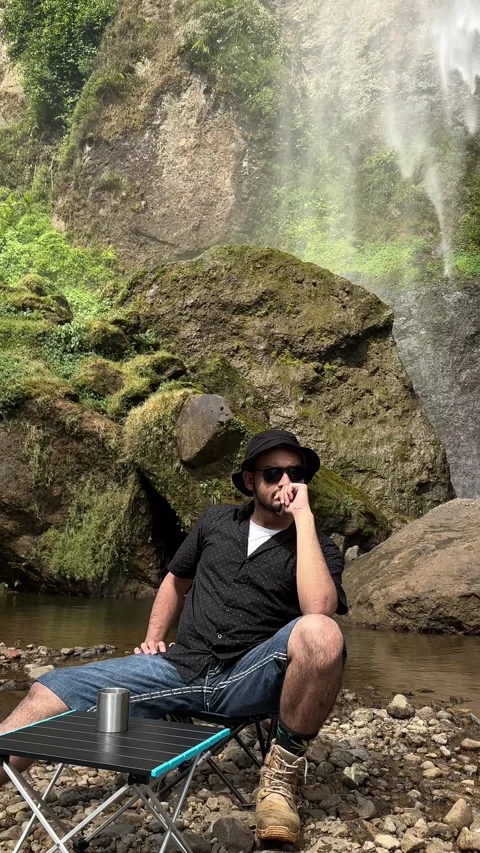 Man Camping at Waterfall then Vertical Pan Up to Large Natural Waterfall Stock Footage 323912062