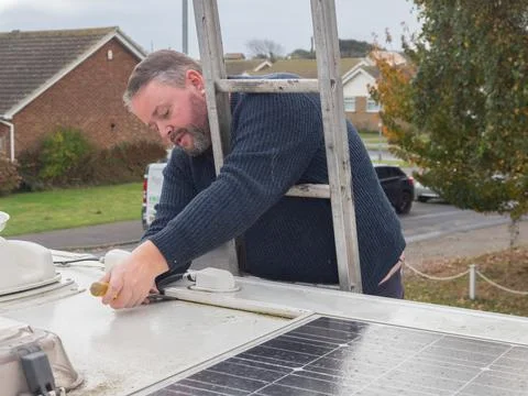 A man can be seen working from a ladder to remove plastic ducting from the roof Stock Photos