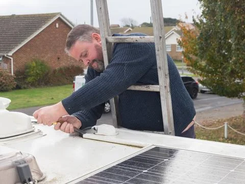 A man can be seen working from a ladder to remove plastic ducting from the roof  Stock Photos