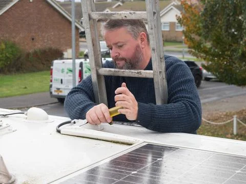 A man can be seen working from a ladder to remove plastic ducting from the roof  Stock Photos