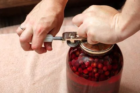 A man canning cherry compote using a manual seaming machine to seal a large 库存照片