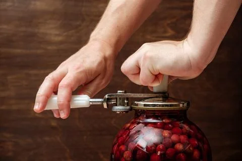 A man canning cherry compote using a manual seaming machine to seal a large Stock Photos