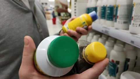 Man can't decide in store what to buy. Close-up hands holding two chemicals 스톡 동영상 220927179