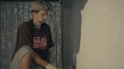 Man in cap carefully paints wall in gray colour Stock Footage 66173832