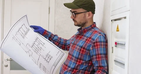 Man in cap examines electric wiring diagram near power panel Video stock 302029693