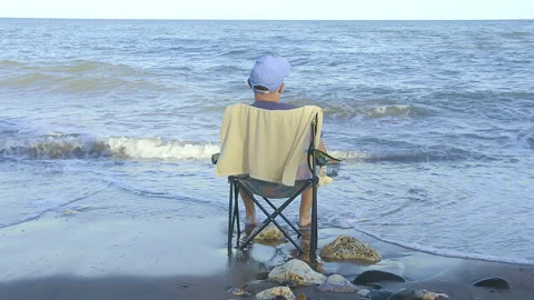Man in cap relaxes sitting on a sandy beach in a folding chair Stock Footage 299708935