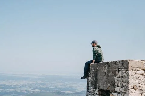 Man with cap  sitting backside looking view from top of building. Stock Photos