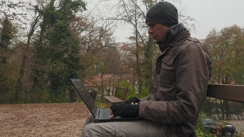 A man with a cap sitting on the bench and working on notebook computer Stock-Footage 98111575