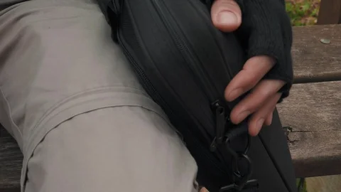 A man with a cap sitting on the bench taking out notebook computer Stock Footage 98111500