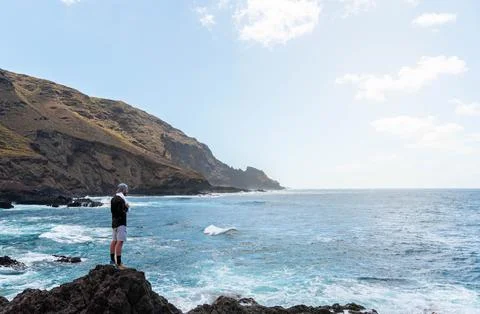 Man with cap standing in the rocks watching the seascape in a clear day Stock Photos
